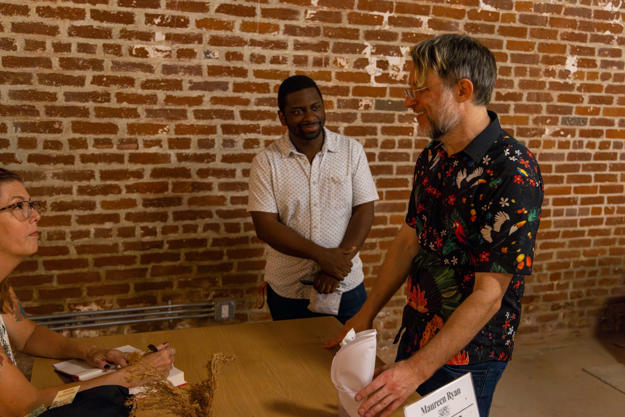 A seated woman looks at a man in front of her, and another standing man looks at the first man as well.