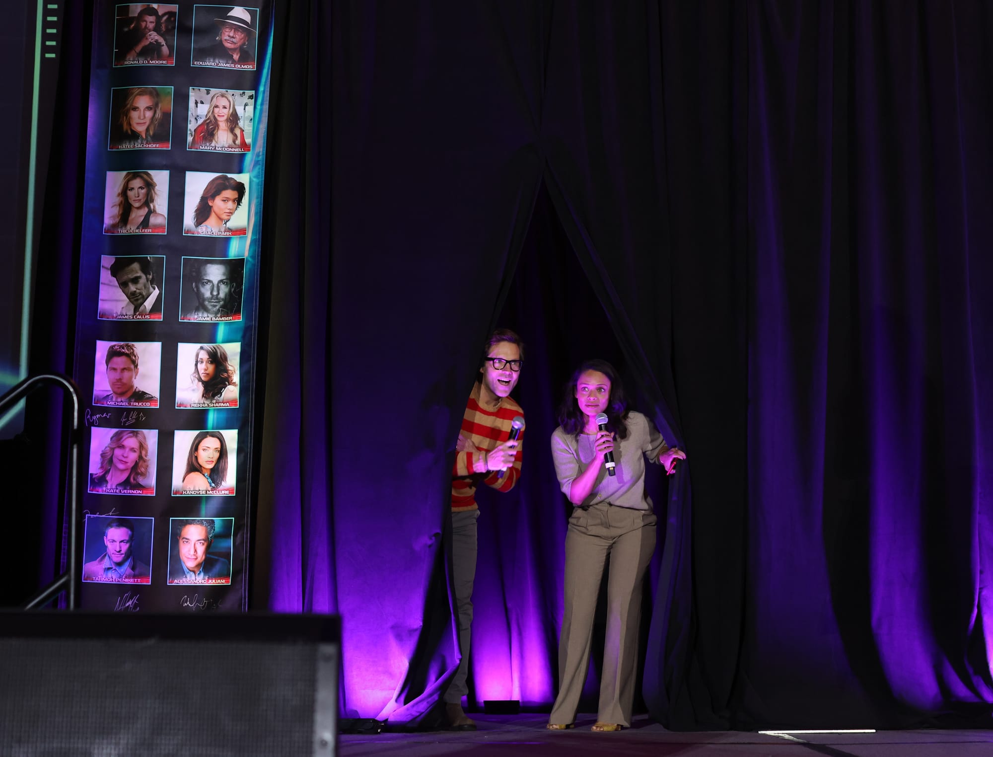 Jamie Bamber and Kandyse McClure peek out from dark curtains on to the stage of the Battlestar Galactica convention.