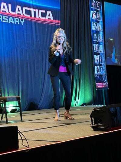 Mary McDonnell standing and smiling on a stage with a blue backdrop.