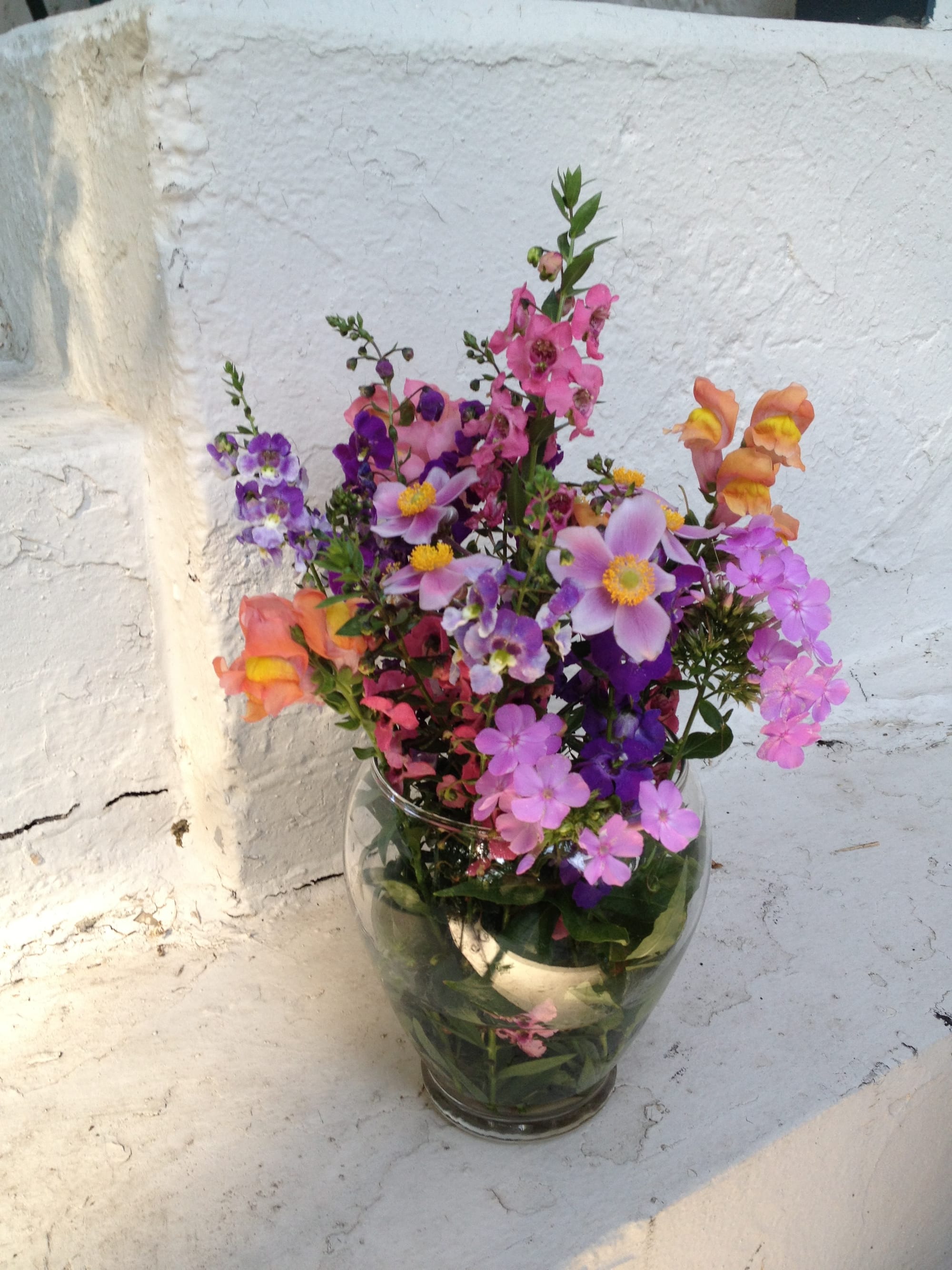 An arrangement of colorful flowers in a clear vase on white steps.