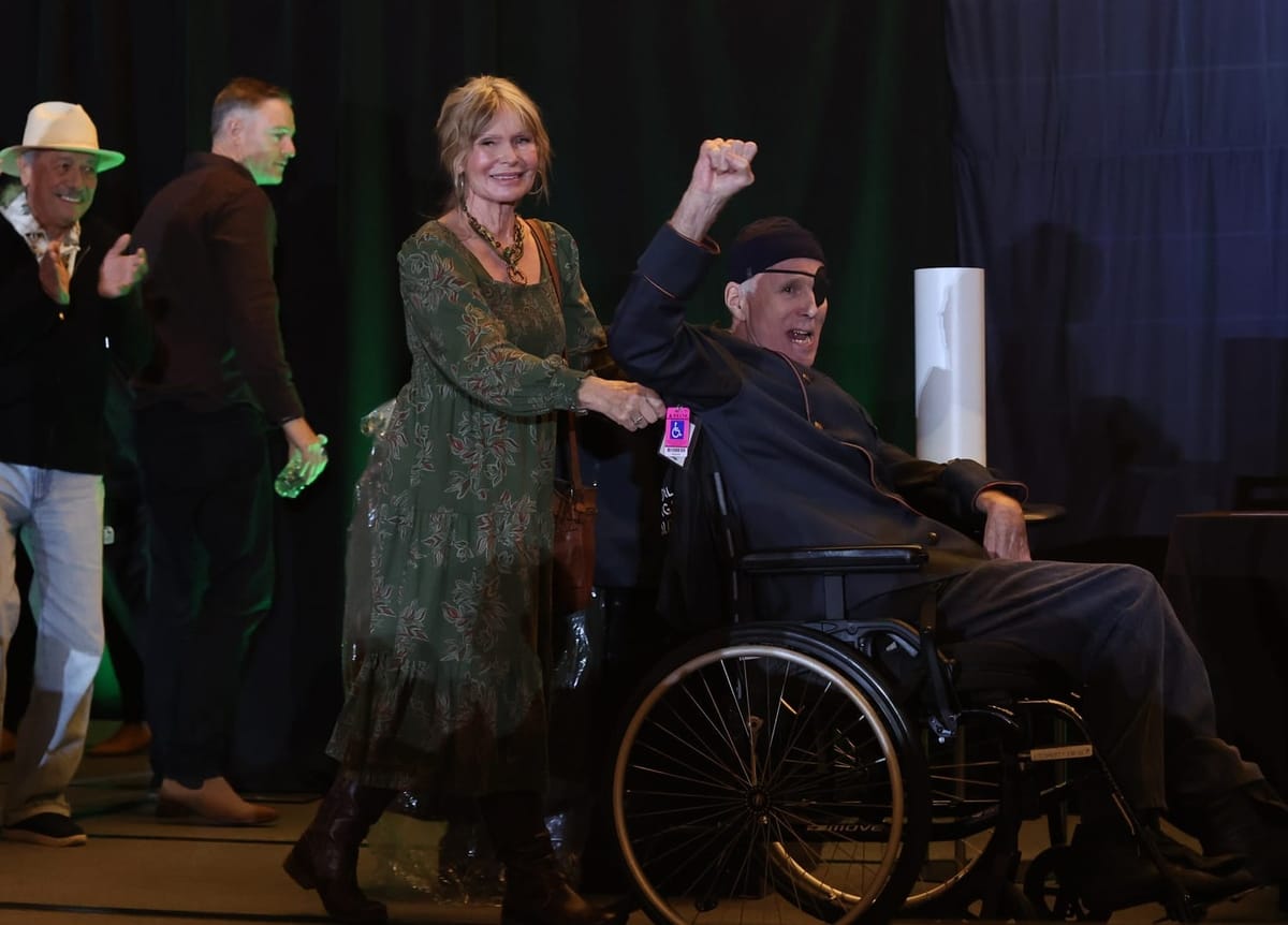 Susan Hogan and Michael Hogan on stage at the BSG con, Hogan's fist is raised.